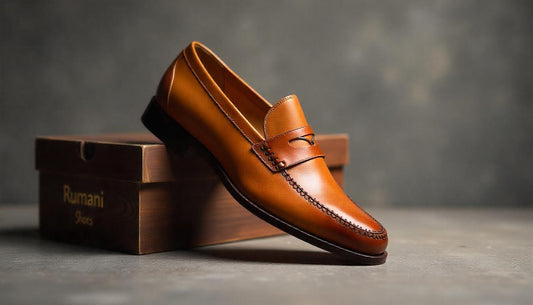 A sophisticated hero shot of a pair of tan brown handcrafted leather loafers from Rumani Shoes, with one shoe elegantly placed on a vintage wooden shoebox.